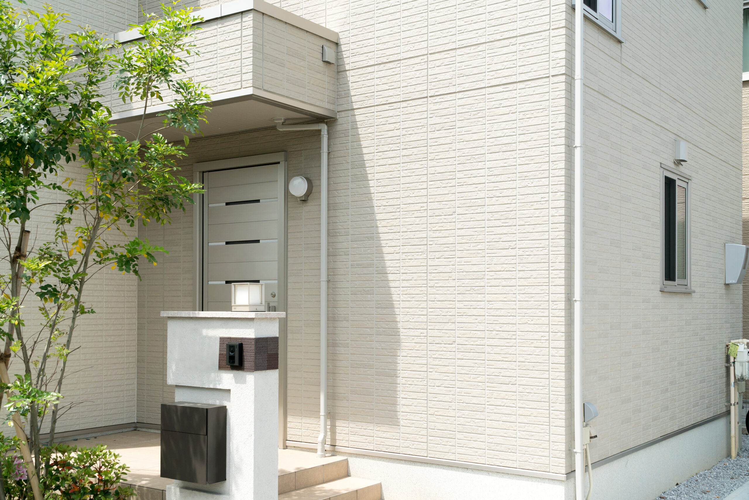 門柱とポスト、植栽まで整った住まいの玄関まわりに朝の光が差している（デモ）