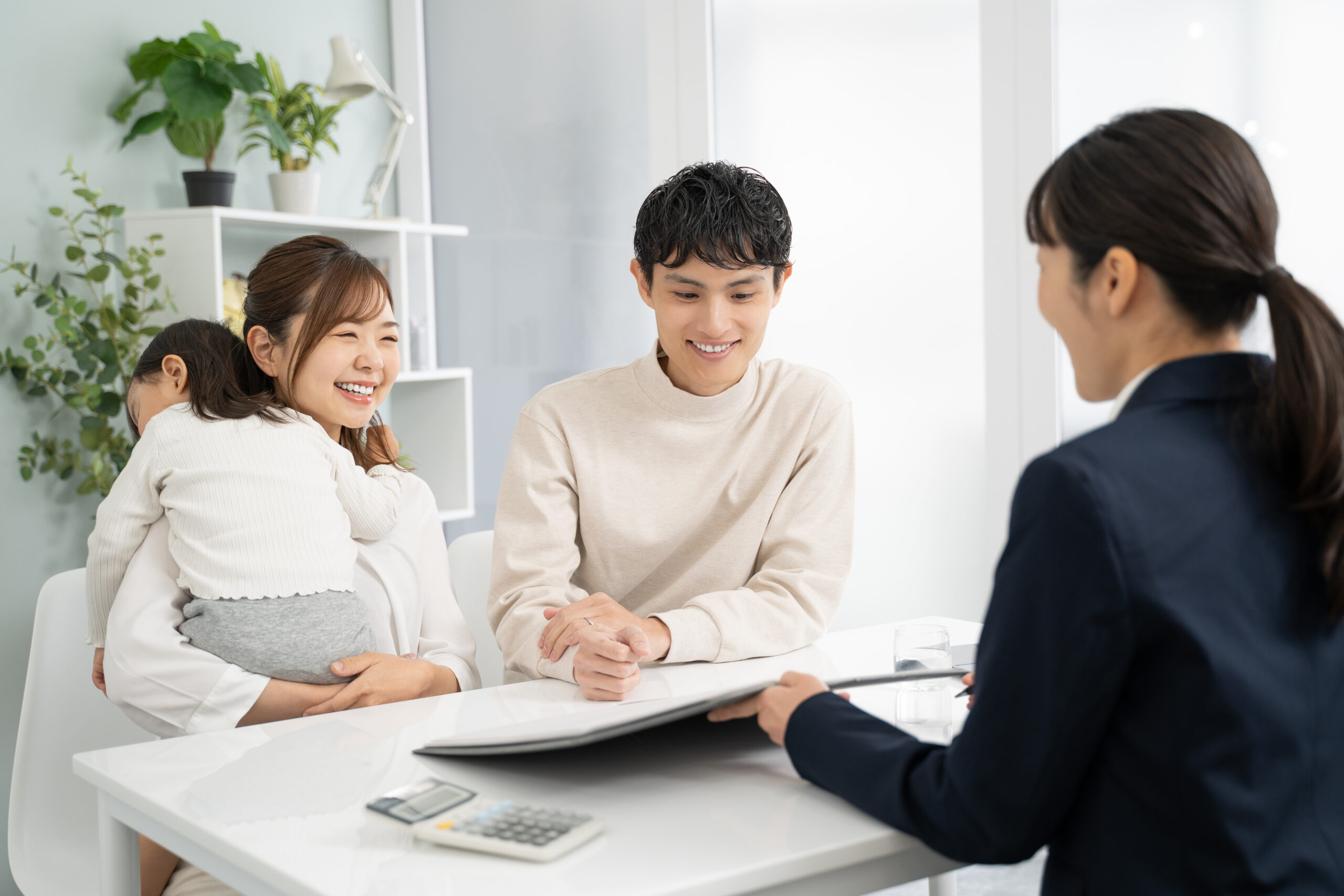ご家族が担当者から書類の説明を受けている。机には電卓と資料が置かれている（デモ）